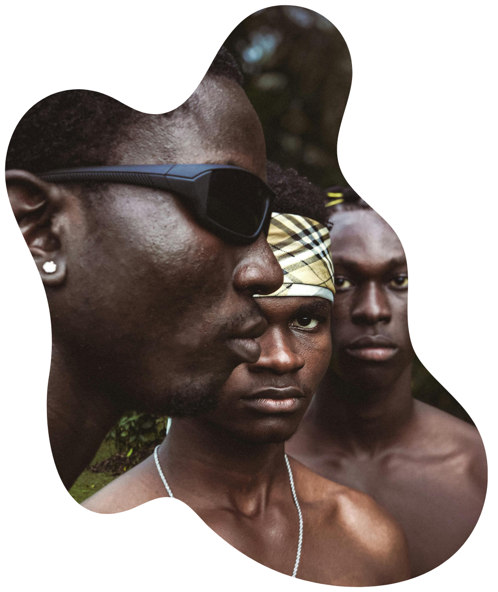 Three Black men standing together in natural light, wearing expressive accessories and intense expressions 