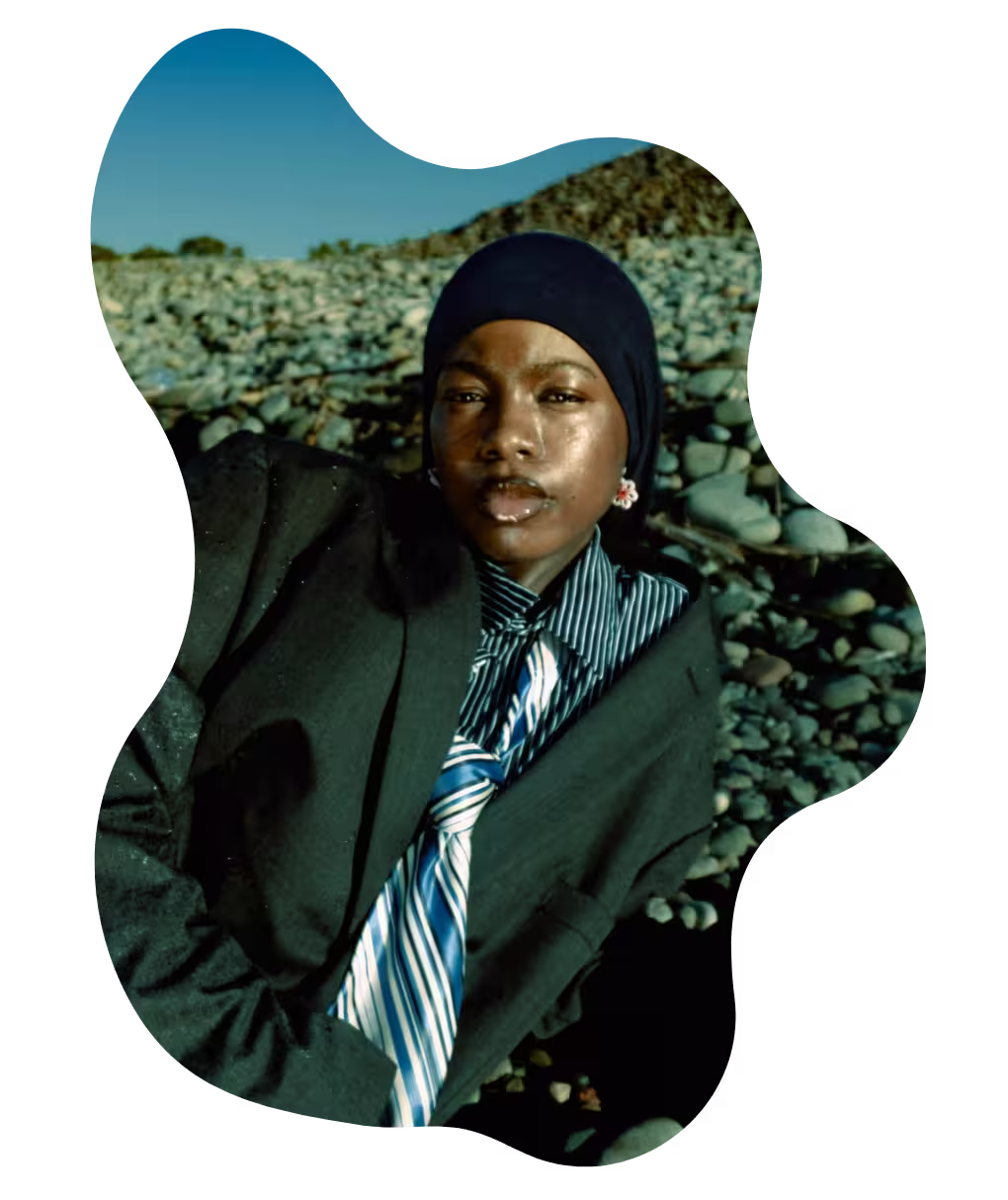 Black creative wearing a suit and hijab, resting on rocky terrain under the sun