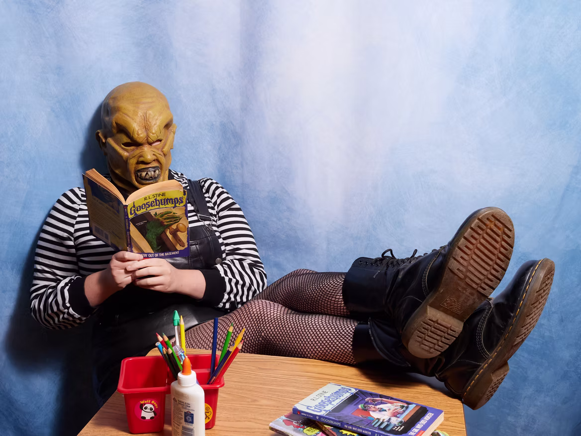 Guest in a horror-inspired costume reading a Goosebumps book at the nostalgic photo booth during the Grown-Up Book Fair.