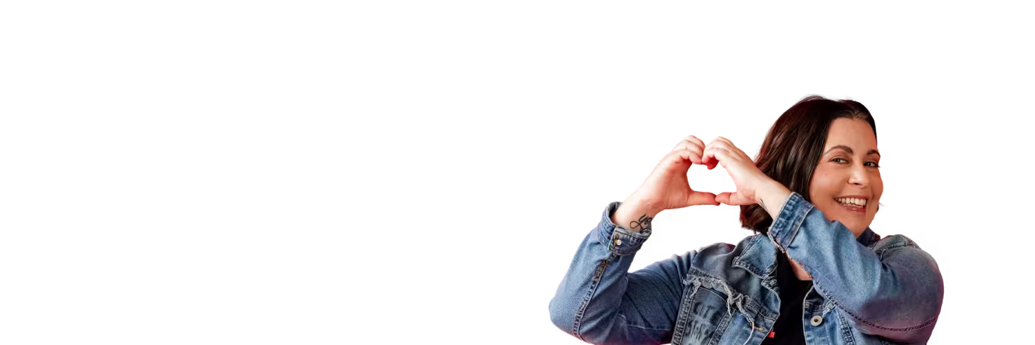 Ryan of Cute Story Events smiling and making a heart shape with their hands while wearing a denim jacket against a black background