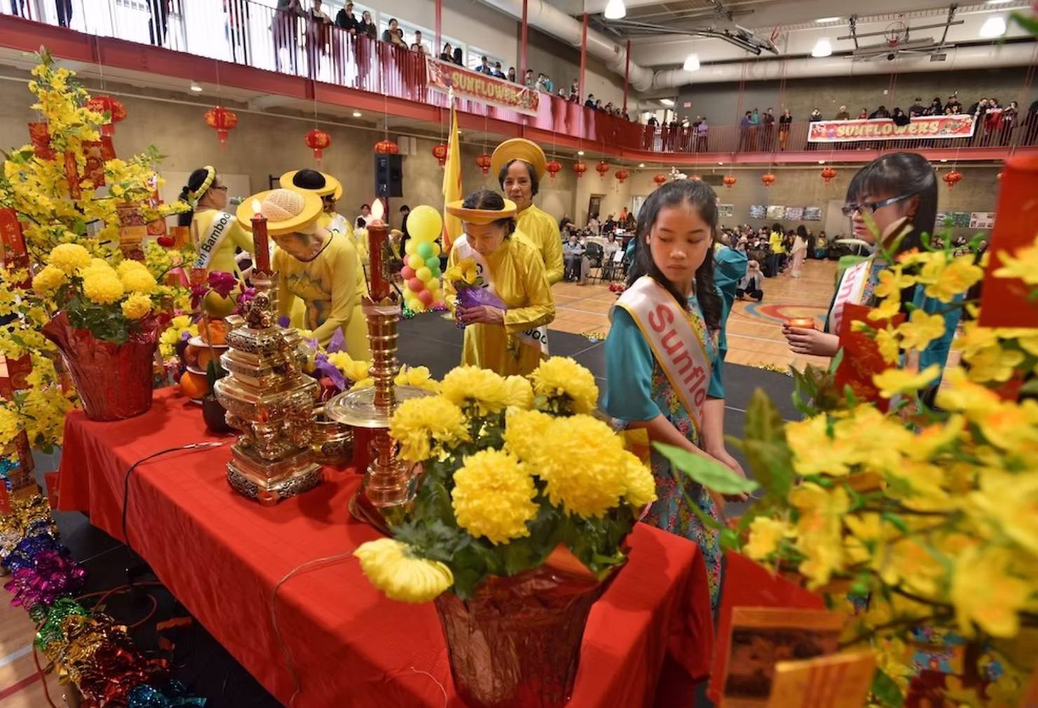 Participants in traditional Vietnamese áo dài dresses gathered around an ancestral altar with flowers, candles, and offerings during a Tet celebration.