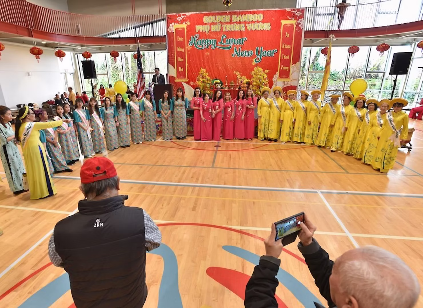 Performers wearing colorful Vietnamese áo dài dresses during a Tet Lunar New Year cultural fashion presentation on stage.