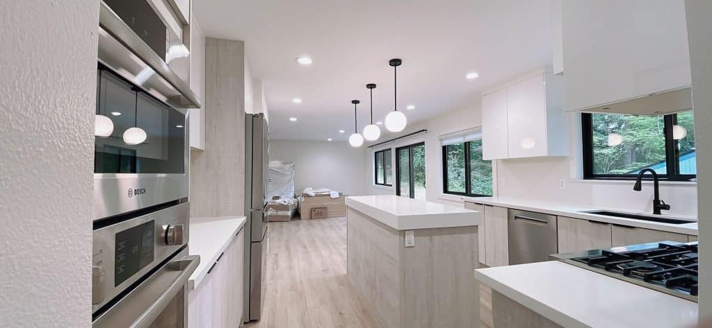 Bright, modern kitchen renovation with white cabinetry, large island, and globe pendant lighting by Iconic Cabinetry.