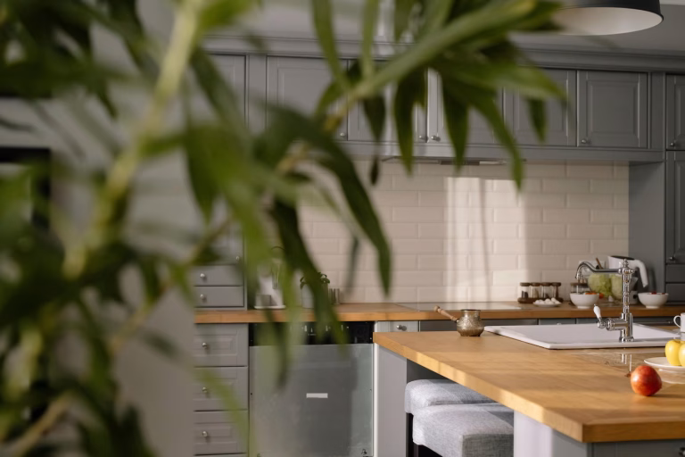 Modern kitchen with white subway tile backsplash and warm wood countertops partially visible through greenery