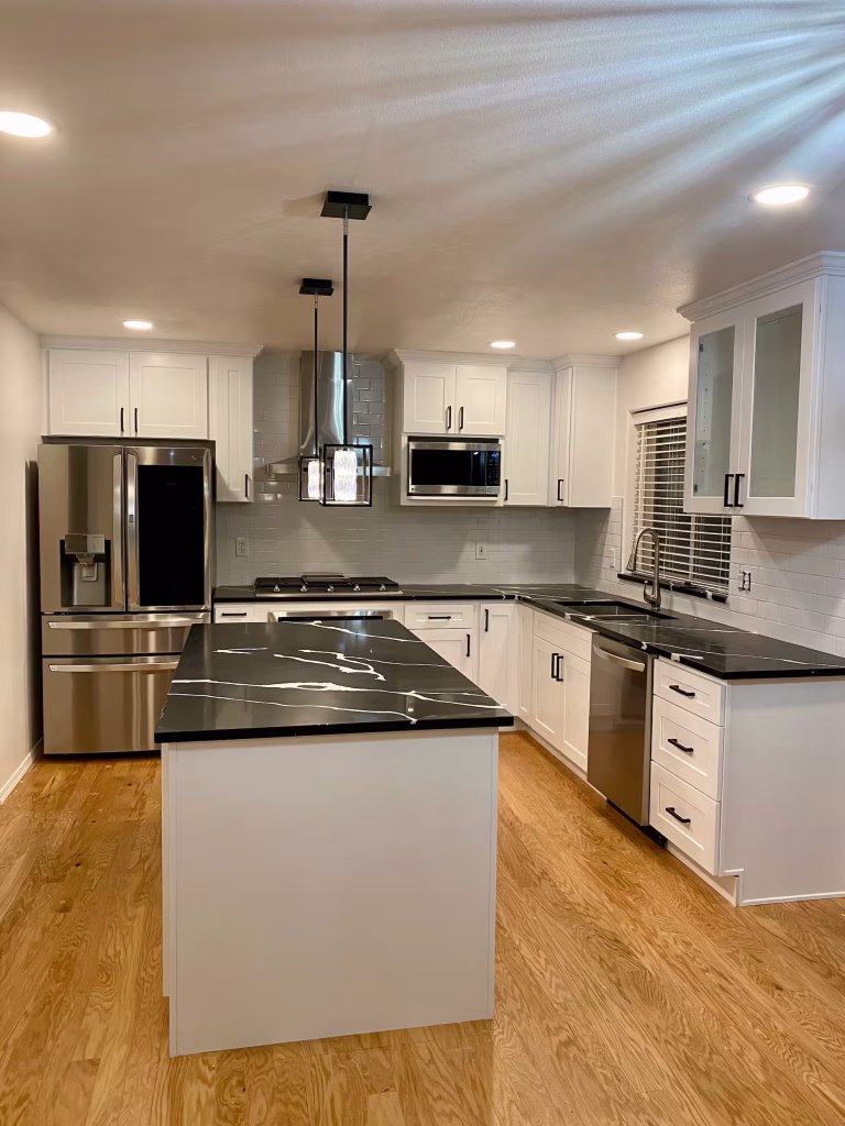 Modern kitchen with white shaker cabinets and striking black marble countertops, featuring stainless steel appliances and wood flooring