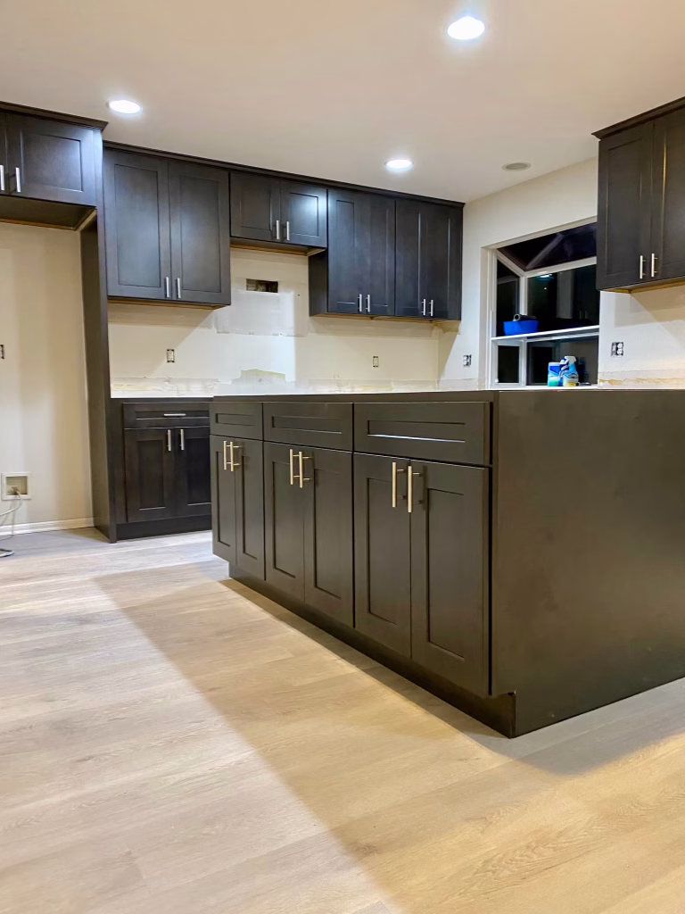 Spacious kitchen installation with matte black shaker cabinets, brushed nickel hardware, and light wood flooring under bright recessed lighting
