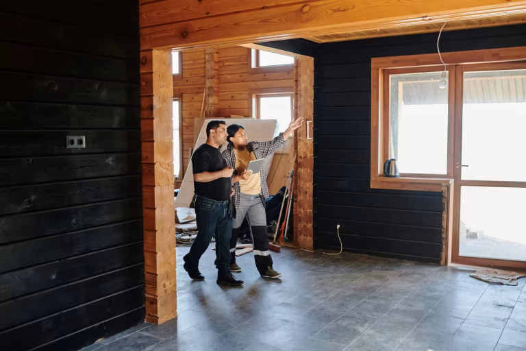 Two construction professionals discussing renovation plans inside a wood-paneled home with exposed beams and partially completed interior work