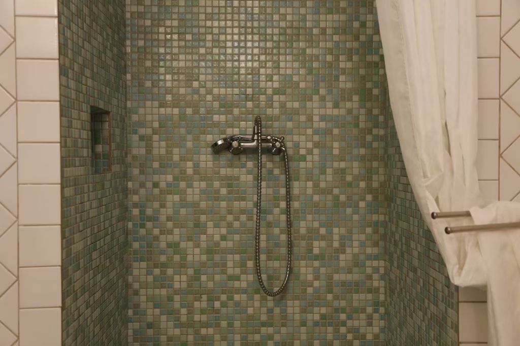 A bathroom remodel in Mountlake Terrace, WA, featuring beautiful green tile and a showerhead.