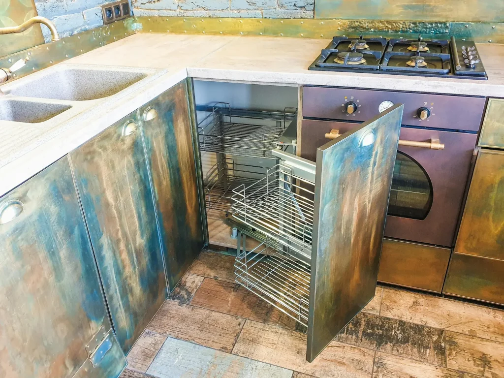 Modern kitchen with patina-style cabinetry and open wire corner drawer, showcasing 2026’s tonal hardware trend